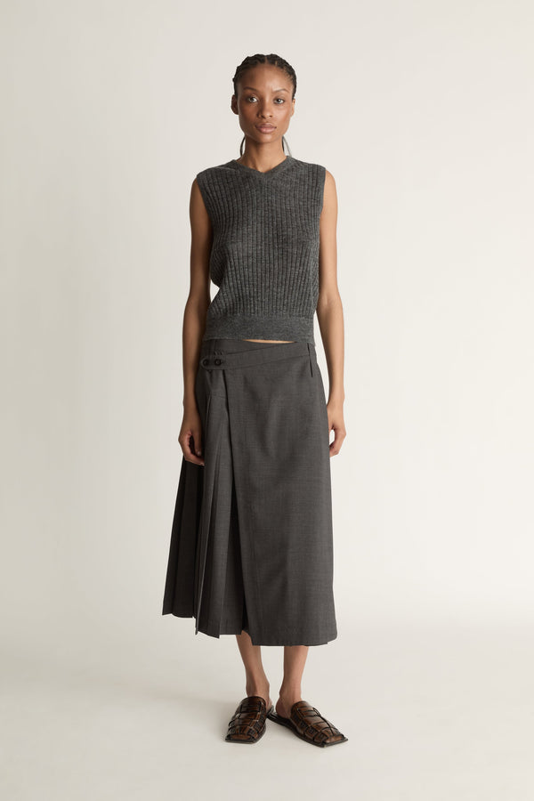 Woman wearing a dark gray sleeveless v neck knit top and skirt on a white background