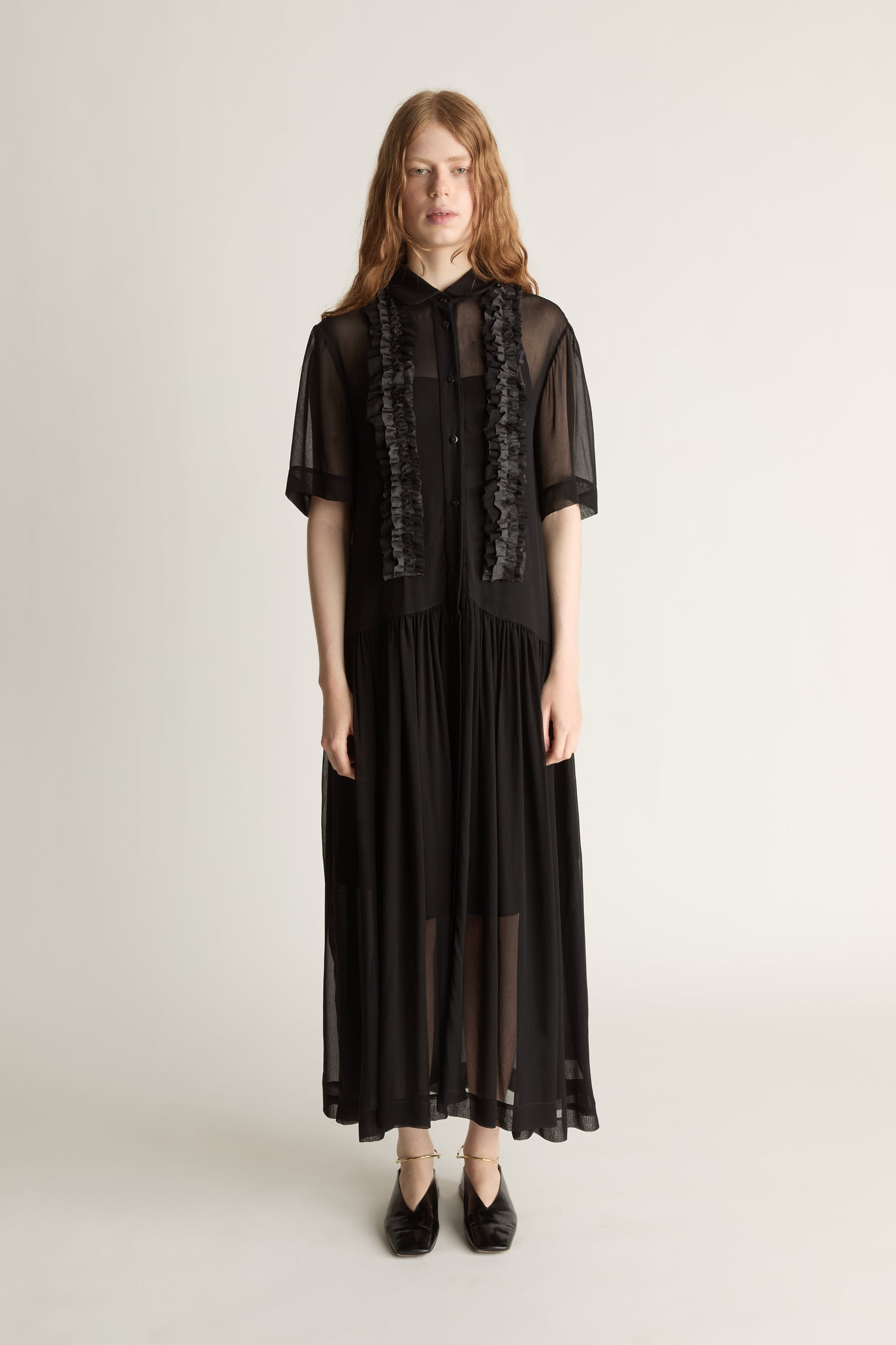 Woman wearing a black dress with sheer sleeves and lace details on a white background