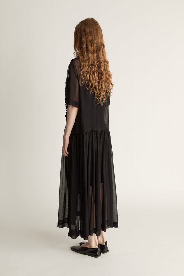 Woman wearing a black dress with sheer sleeves and lace details on a white background