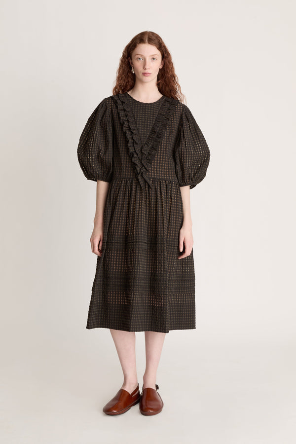 Woman wearing a dark checkered dress  with puffy sleeves with ruffled details on a white background