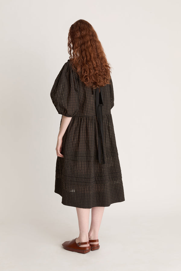 Woman wearing a dark checkered dress  with puffy sleeves with ruffled details on a white background
