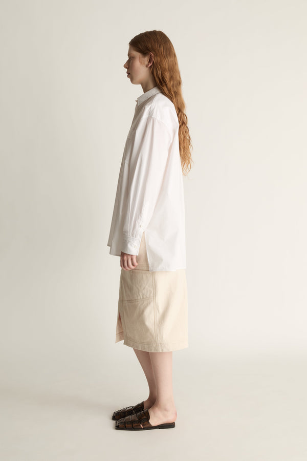 Person wearing a white shirt and beige skirt on a plain background