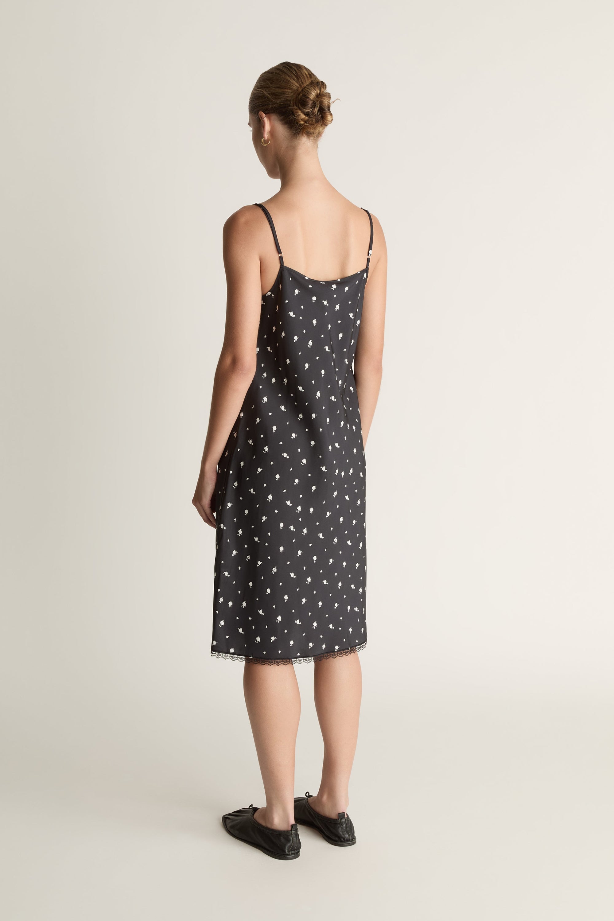Woman wearing a black slip dress with white floral print on a plain background