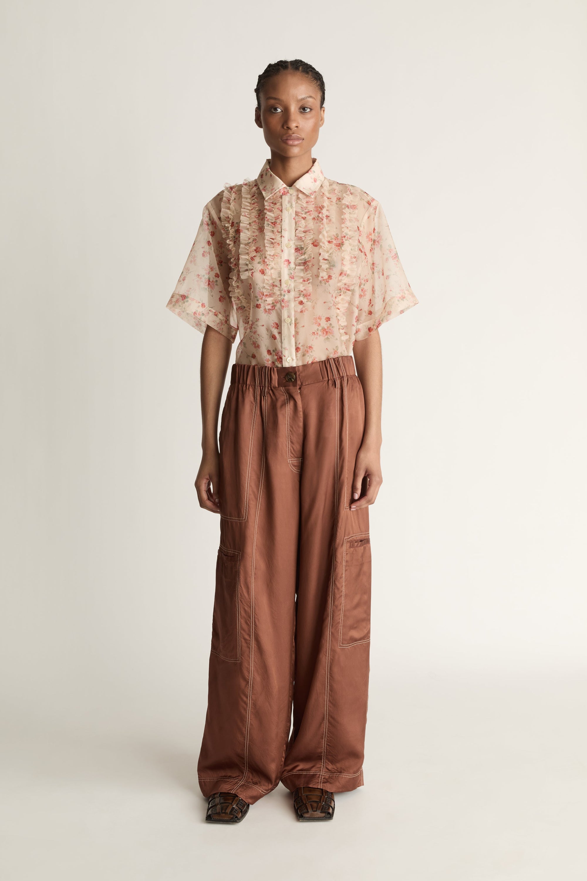 Person wearing a floral blouse and brown pants on a white background