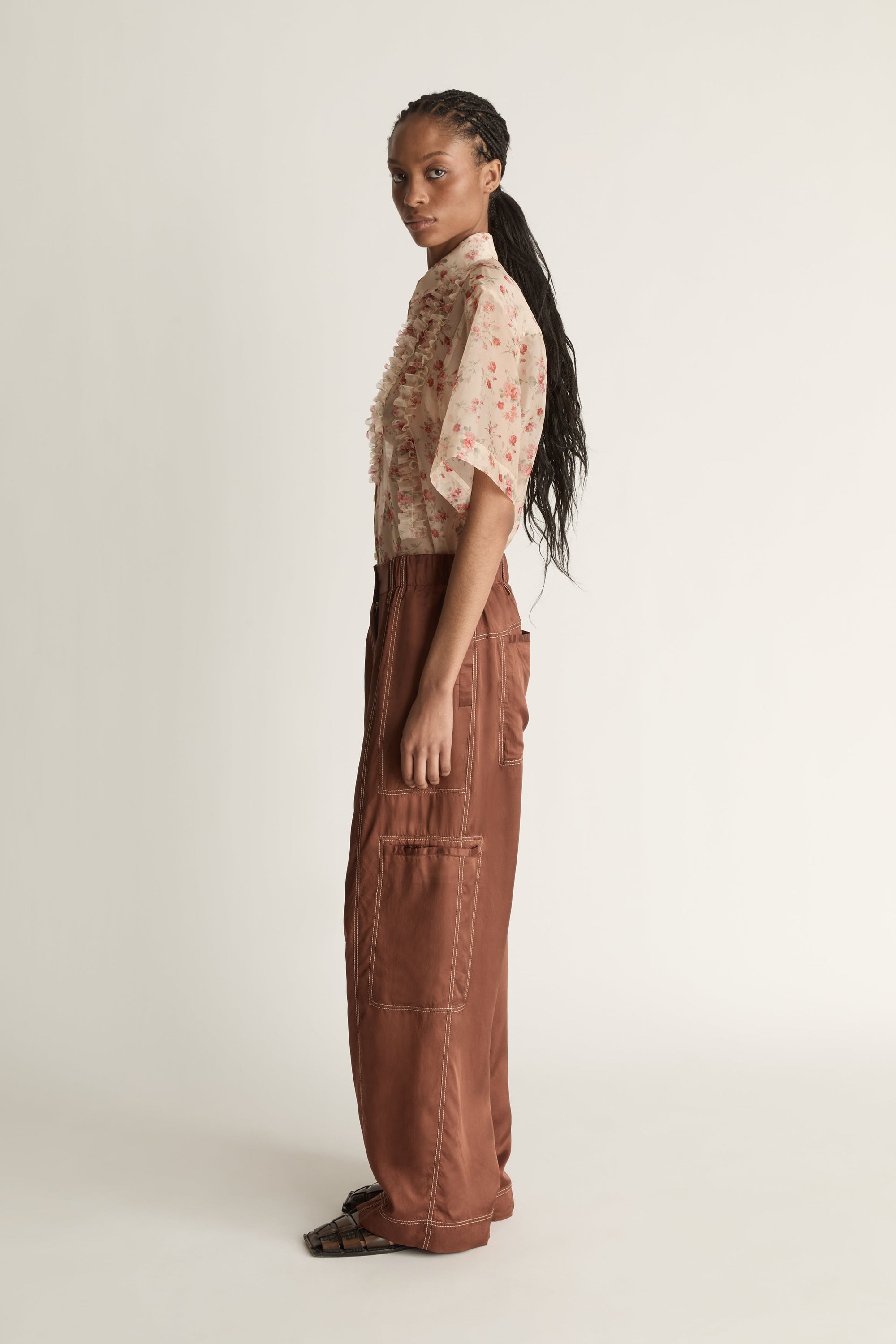 Person wearing a floral blouse and brown pants on a white background
