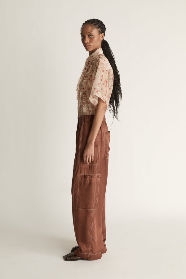 Person wearing a floral blouse and brown pants on a white background