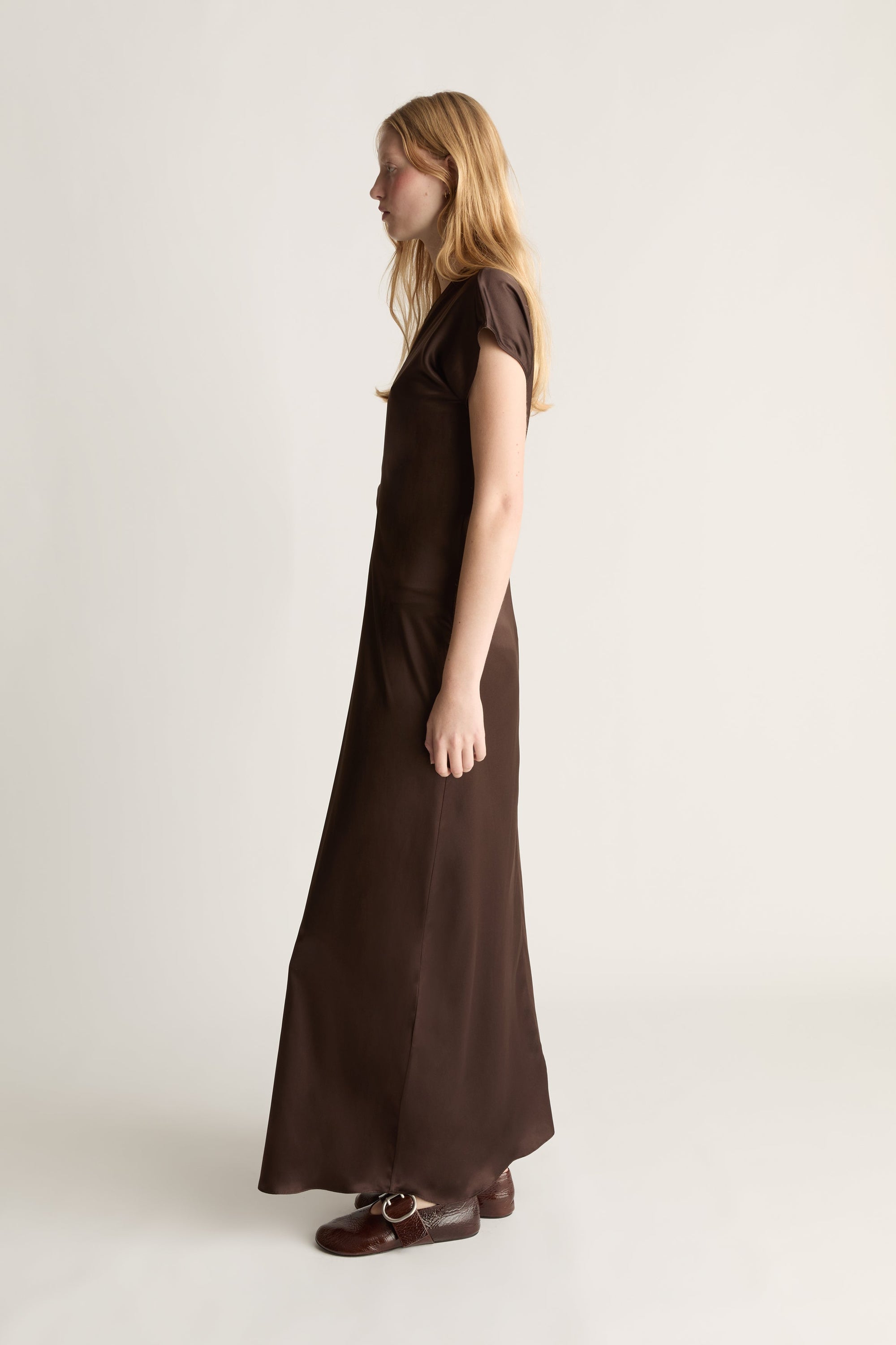 Side view of a woman wearing a long brown dress on a white background