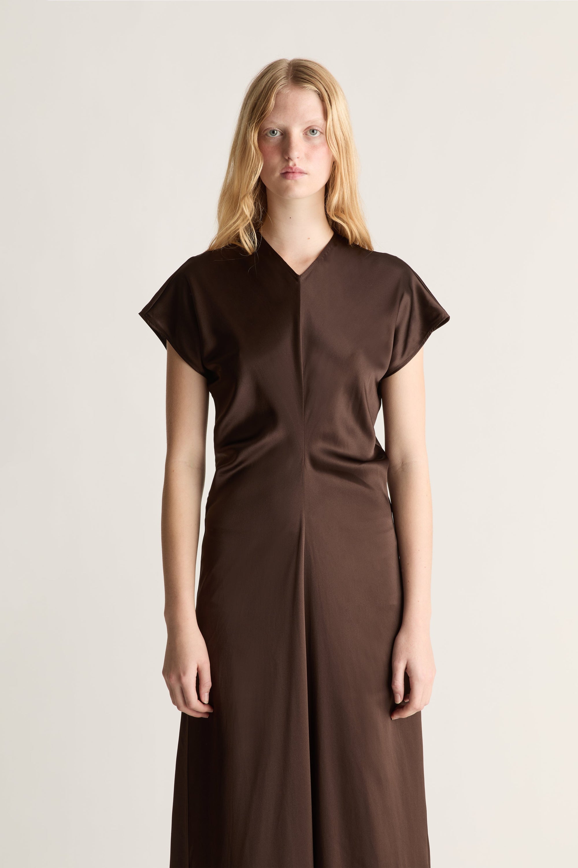 Close up of a woman wearing a brown silk short sleeve dresss against a white studio background.