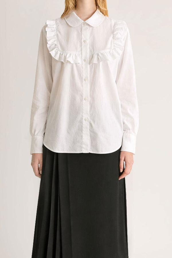 Close up of a woman wearing a white button up cotton shirt with frill detail and a black skirt. 