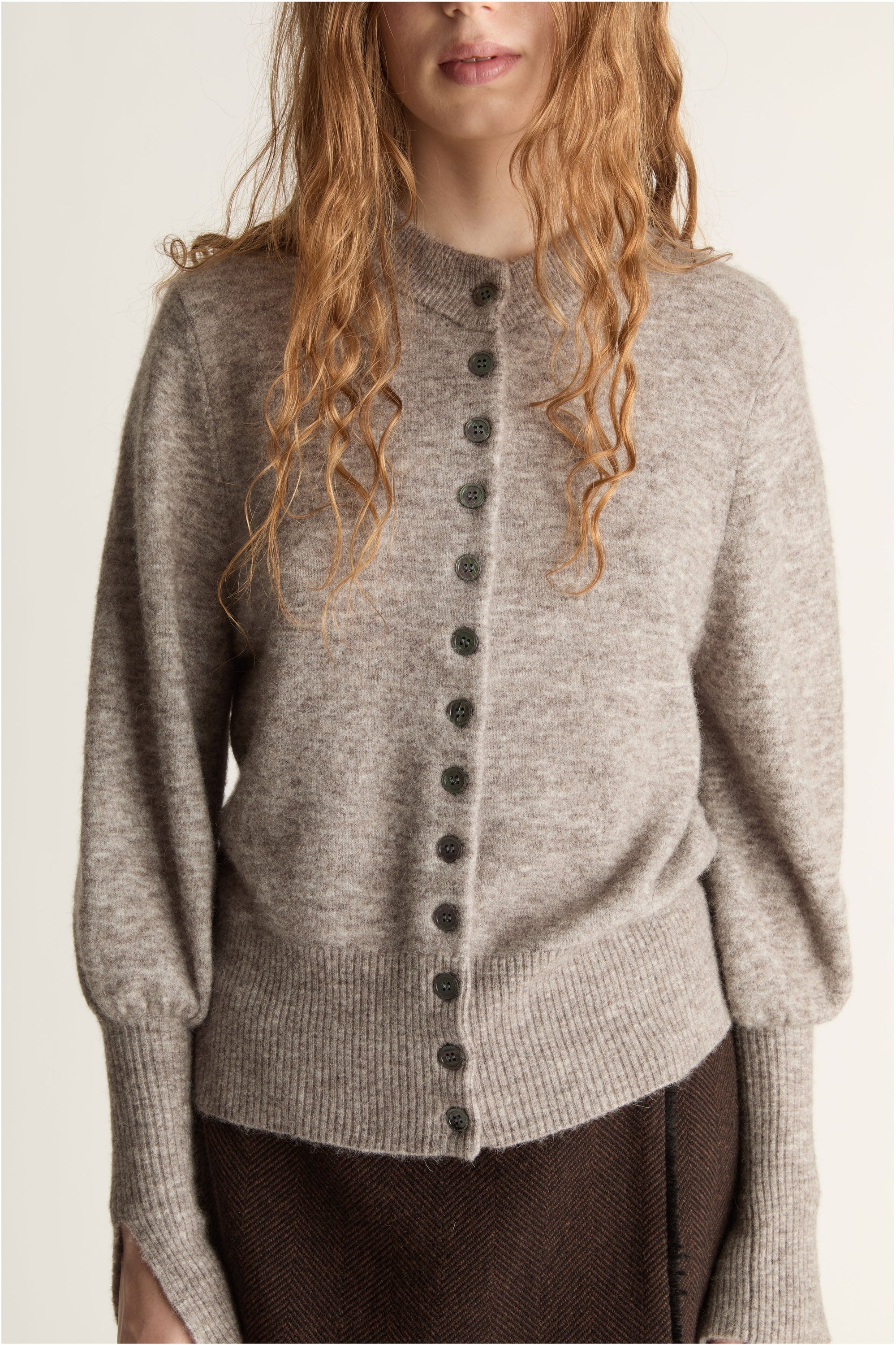 Woman wearing a gray sweater and brown skirt on a plain background